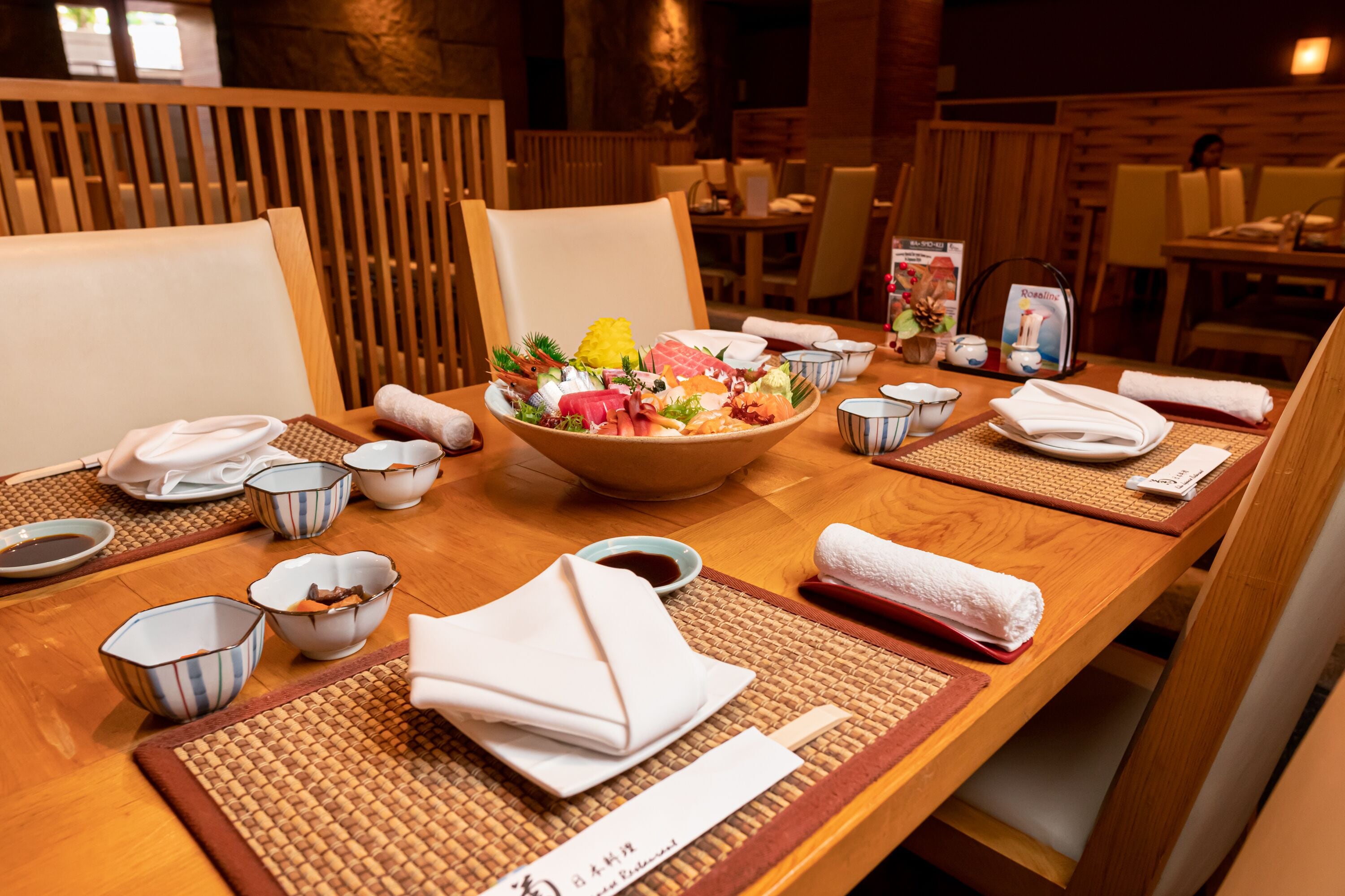 Een eettafel gedekt met een schaal diverse gerechten, kommen, stokjes en servetten.