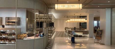 A modern restaurant interior with a central counter, seating area, and a sign reading "DOK CHAMPA restaurant".