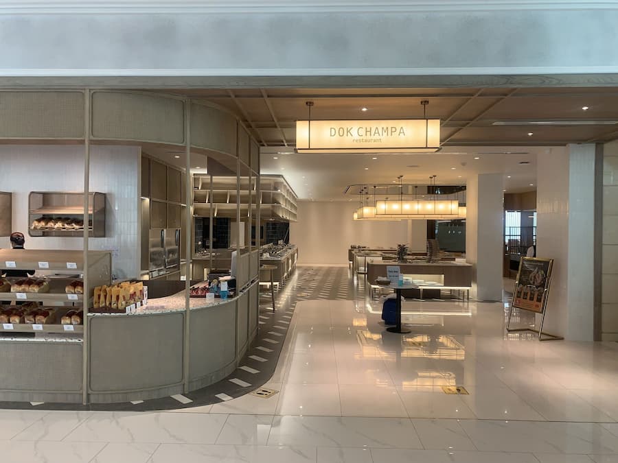 A modern restaurant interior with a central counter, seating area, and a sign reading "DOK CHAMPA restaurant".