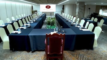 Un salón de conferencias con una larga mesa, sillas blancas y una pantalla que muestra el nombre del hotel.