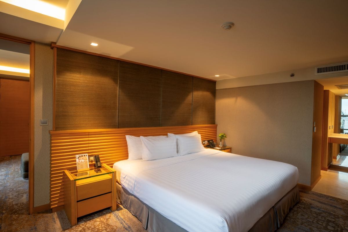 Una habitación de hotel con una cama grande, mesitas de noche, un cabecero de madera y suelo alfombrado.