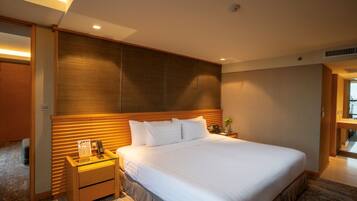 Una habitación de hotel con una cama grande, mesitas de noche, un cabecero de madera y suelo alfombrado.