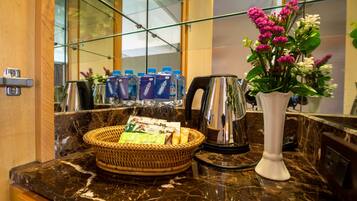 A marble countertop with a wicker basket containing snacks, a white vase with flowers, and a coffee maker.