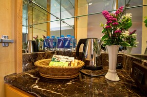 A marble countertop with a wicker basket containing snacks, a white vase with flowers, and a coffee maker.