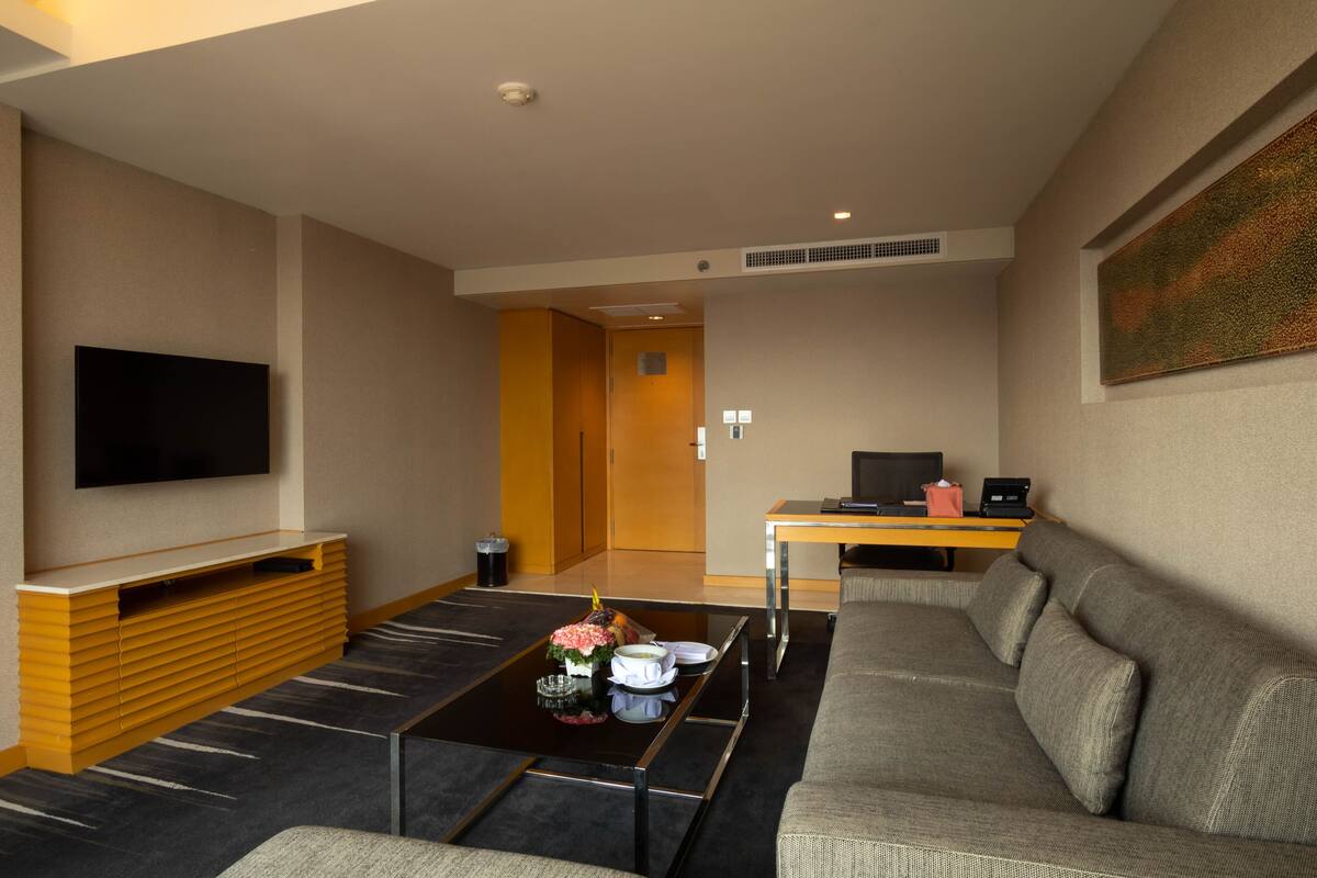 A modern living room with a sofa, coffee table, TV, and a small dining area.