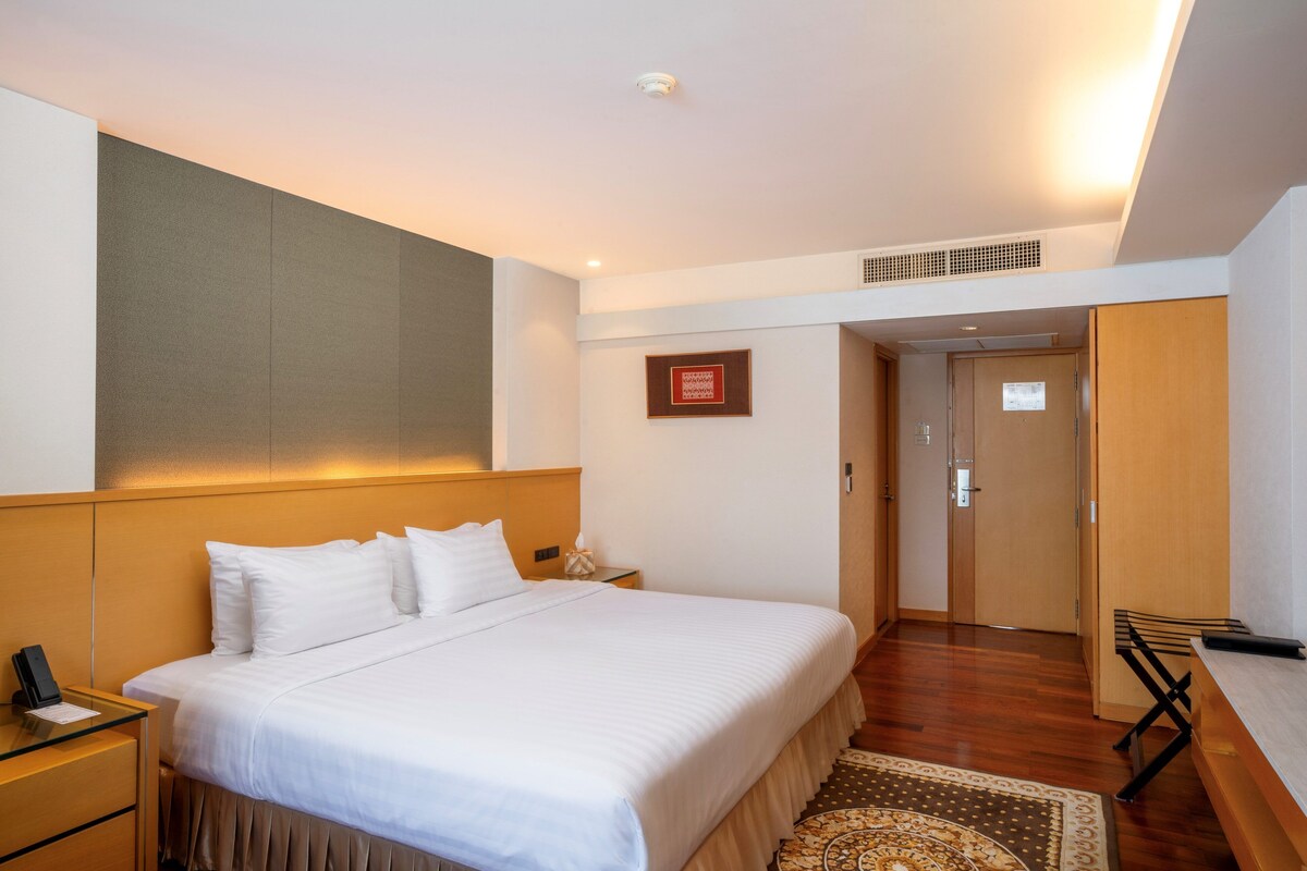 A hotel room with a bed, bedside table, and a desk with a chair.