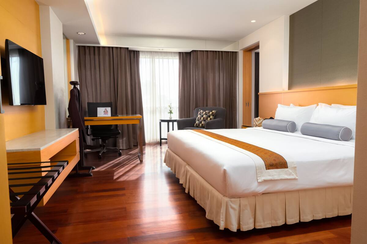 A hotel room with a large bed, a desk with a chair, a television, and a window with curtains.