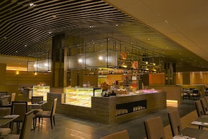 Ein modernes Restaurant mit einer zentralen Theke, auf der Speisen präsentiert werden, umgeben von Esstischen und Stühlen.