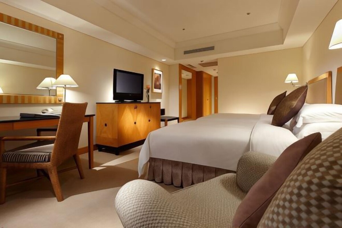 A hotel room with a bed, a desk, a chair, a television, and a large mirror.