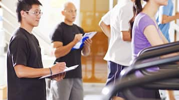 Personer som använder löpband i ett gym med en modern inredning och en stor skärm i bakgrunden.