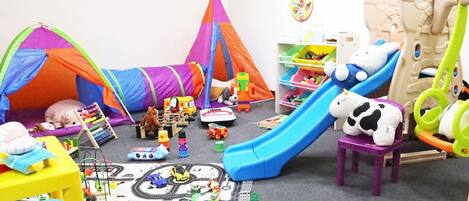 A playroom with a train set, a slide, and various toys.
