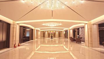 A spacious, well-lit lobby with a reflective floor, a grand chandelier, and a central floral arrangement.