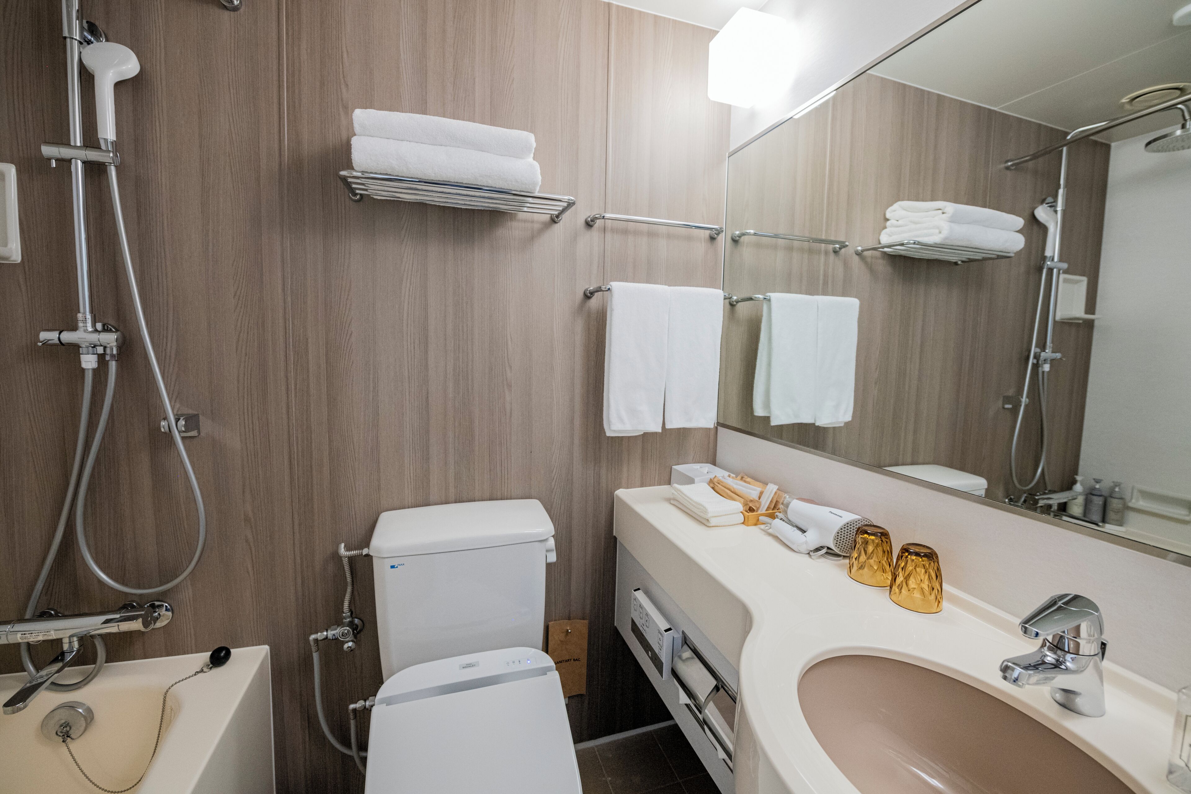 A modern bathroom with a toilet, sink, and shower. There are towels and toiletries on the counter.