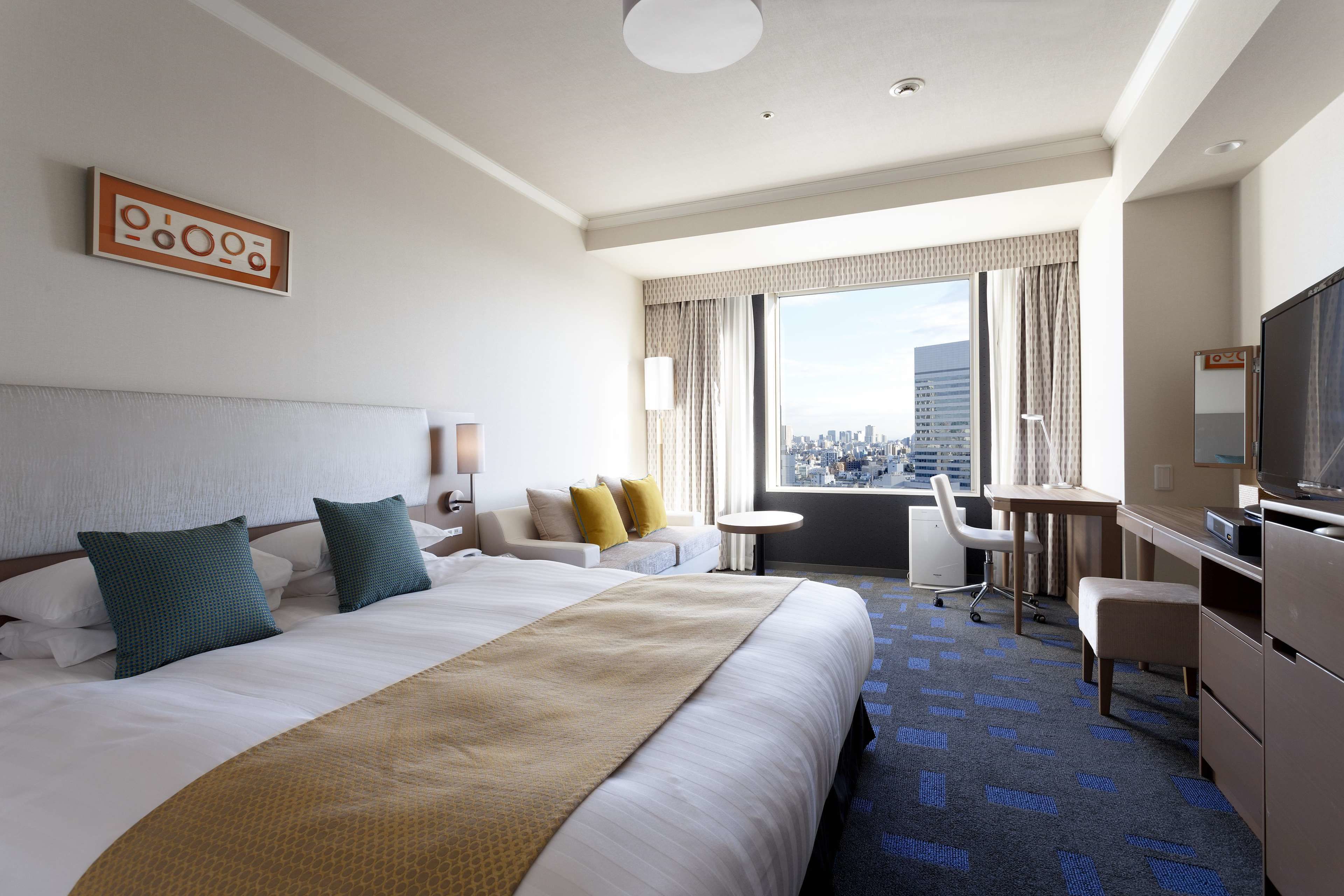 A hotel room with a large bed, a desk, a chair, a TV, and a view of the city.