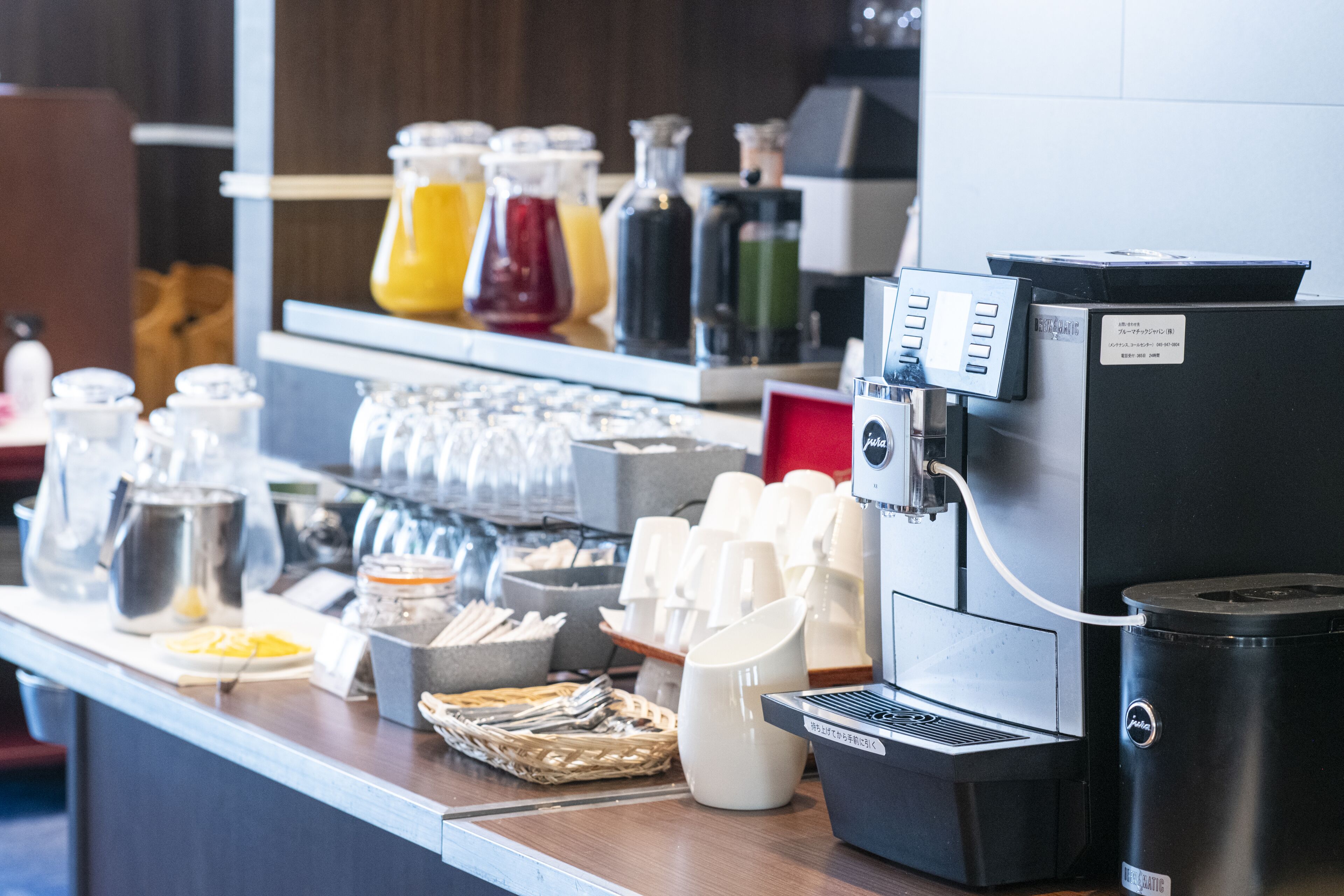 A coffee station with a coffee machine, cups, and various containers of beverages.