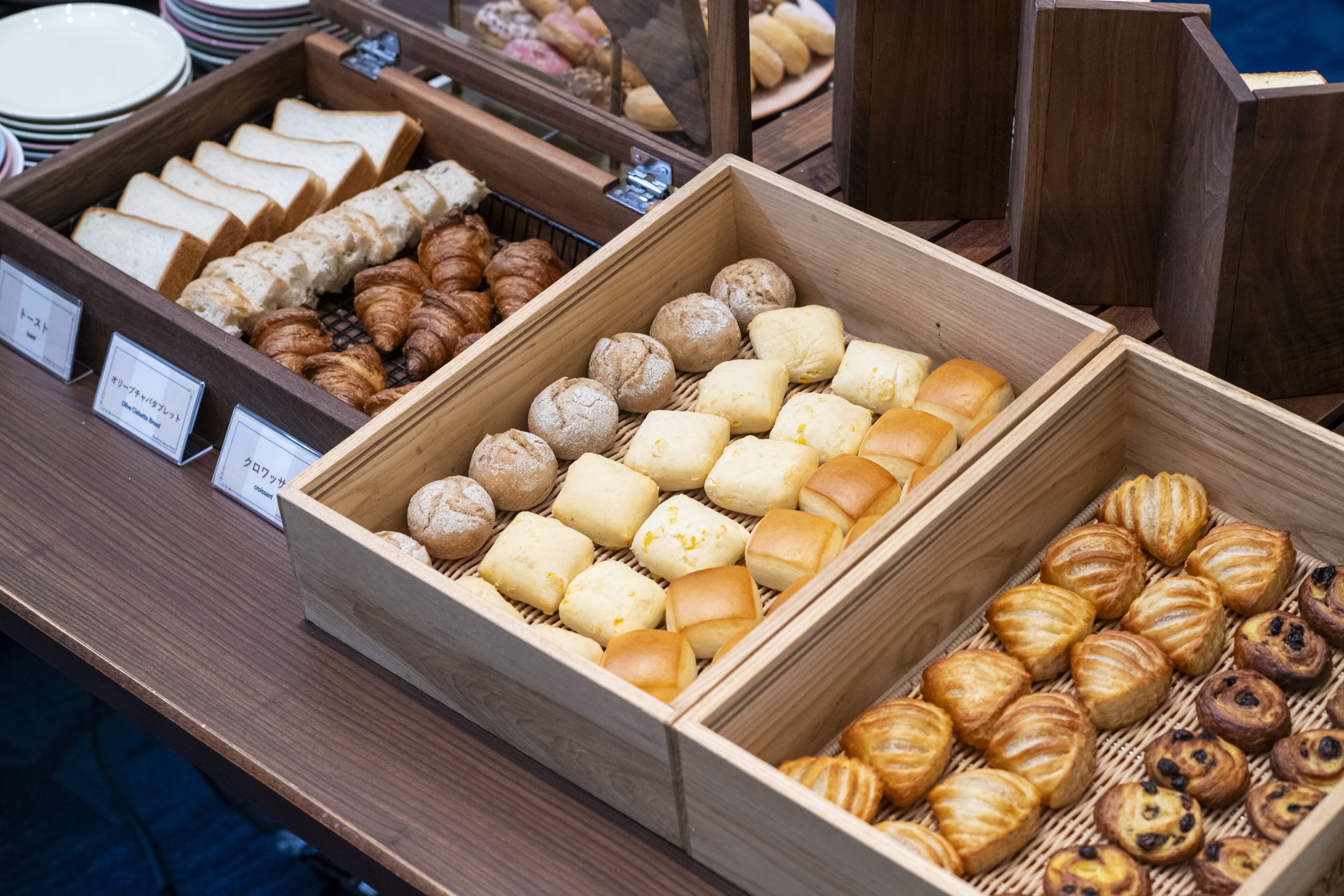Une variété de produits de boulangerie présentés dans des boîtes en bois, notamment du pain, des pâtisseries et des petits pains.