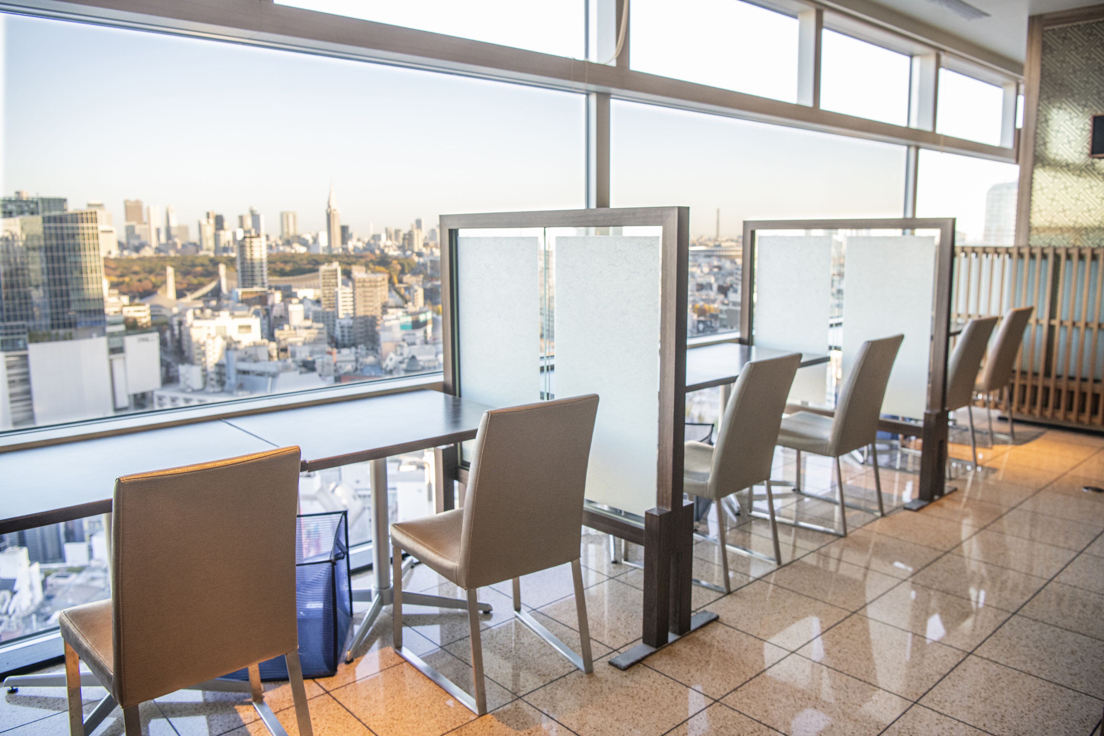A modern office space with large windows offering a city view, several chairs, and a glass partition.