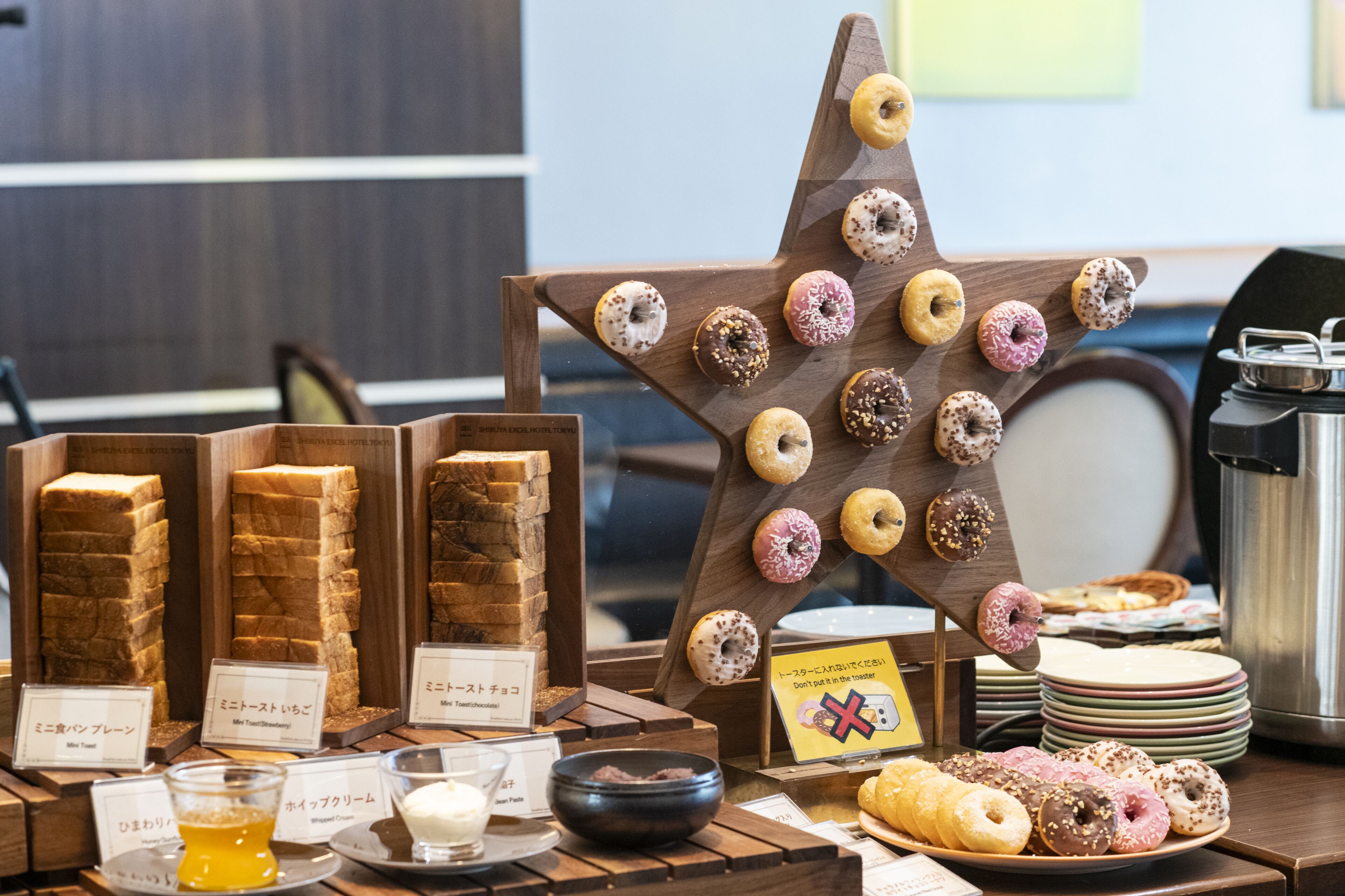 A display of various pastries and desserts, including donuts and bread, arranged on a wooden table with labels.