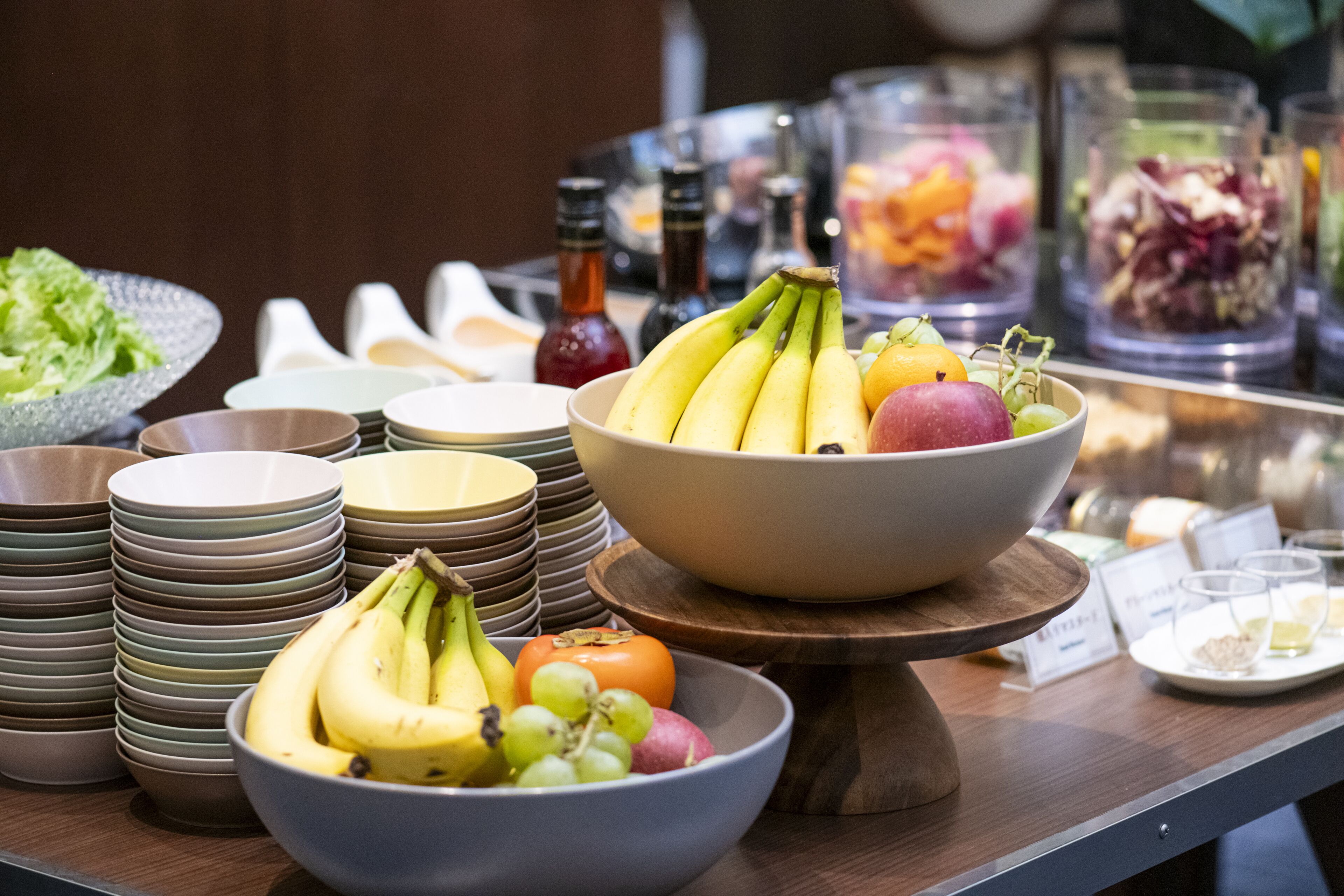 A buffet setup with various fruits and bowls of food, including bananas, apples, and grapes.