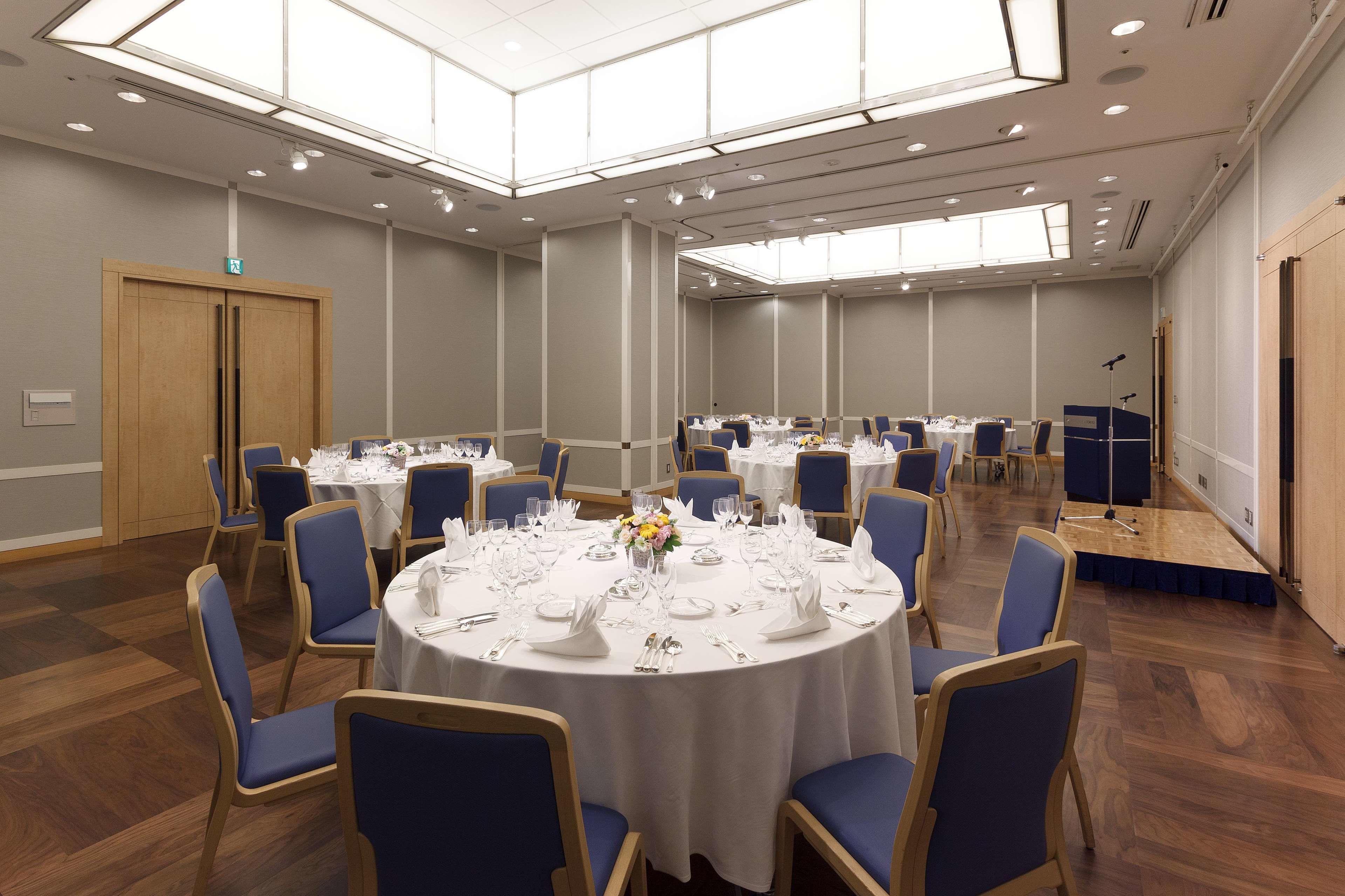 A conference room with round tables, blue chairs, and white tablecloths.