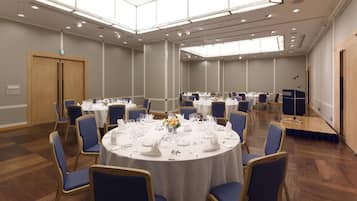 Un salón de conferencias con mesas redondas, sillas azules y manteles blancos.