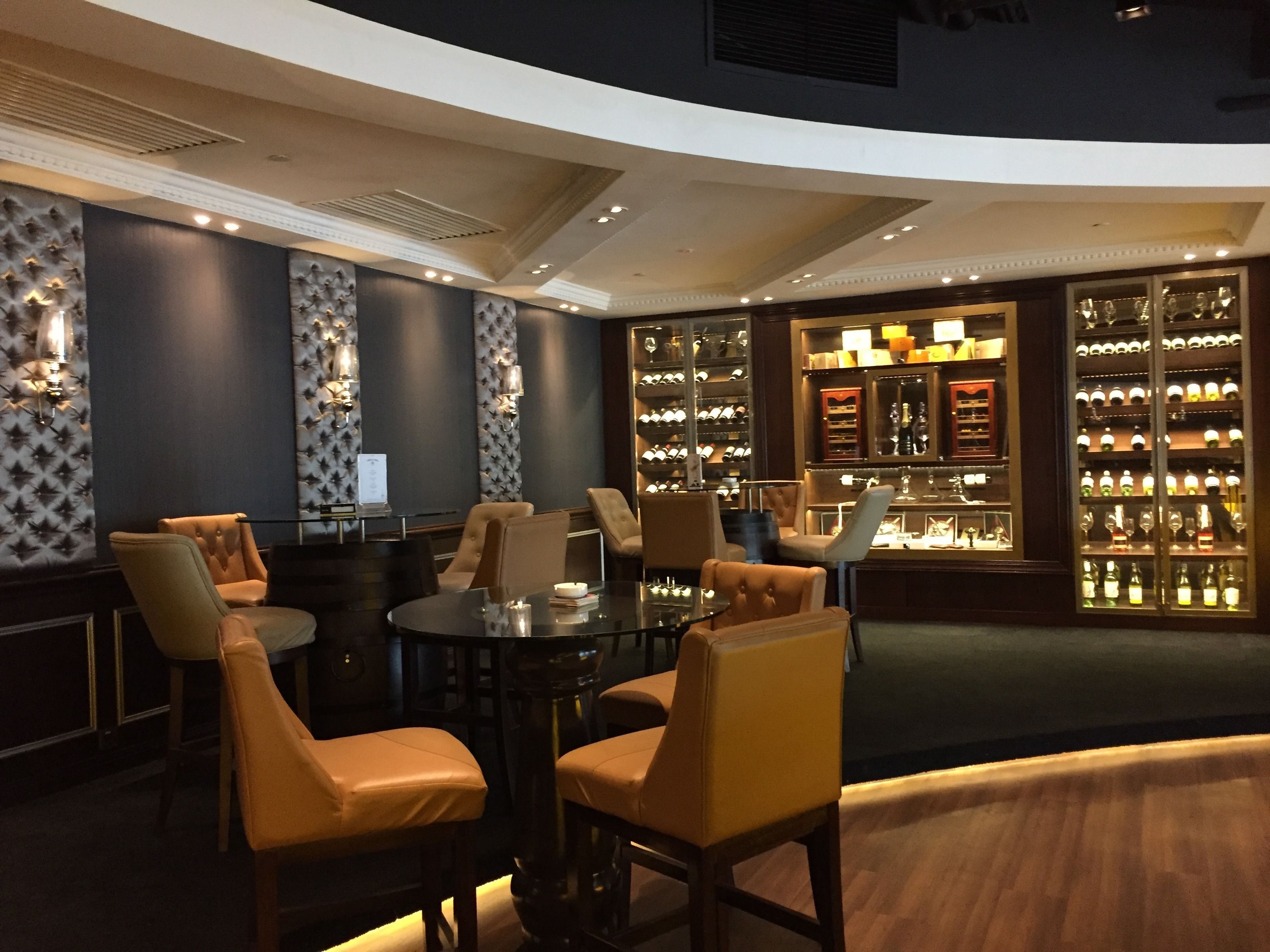 A dimly lit room with a round table surrounded by leather chairs, a wine rack with bottles, and patterned wallpaper.