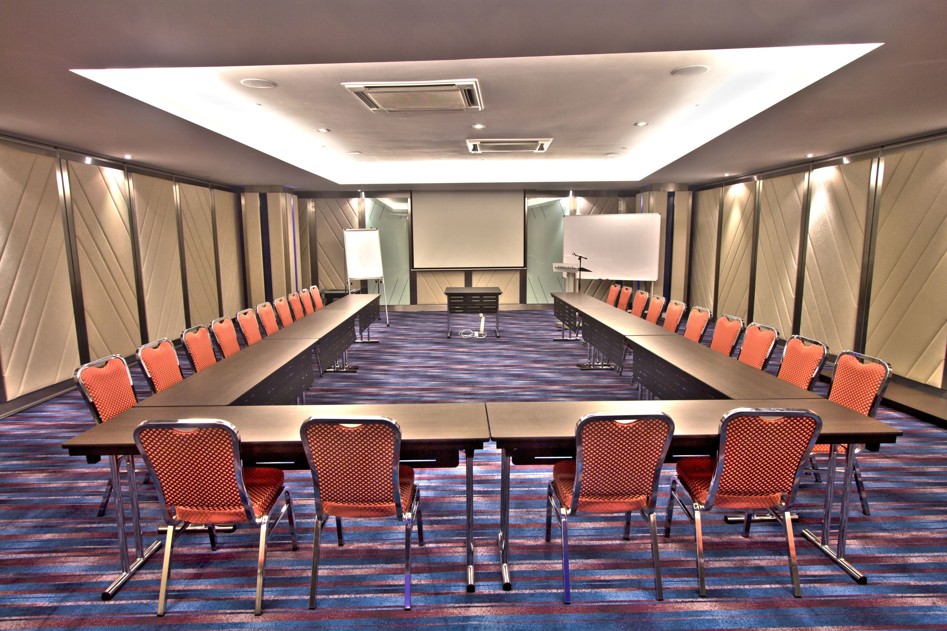 A conference room with a long table, orange chairs, a projector screen, and a carpeted floor.