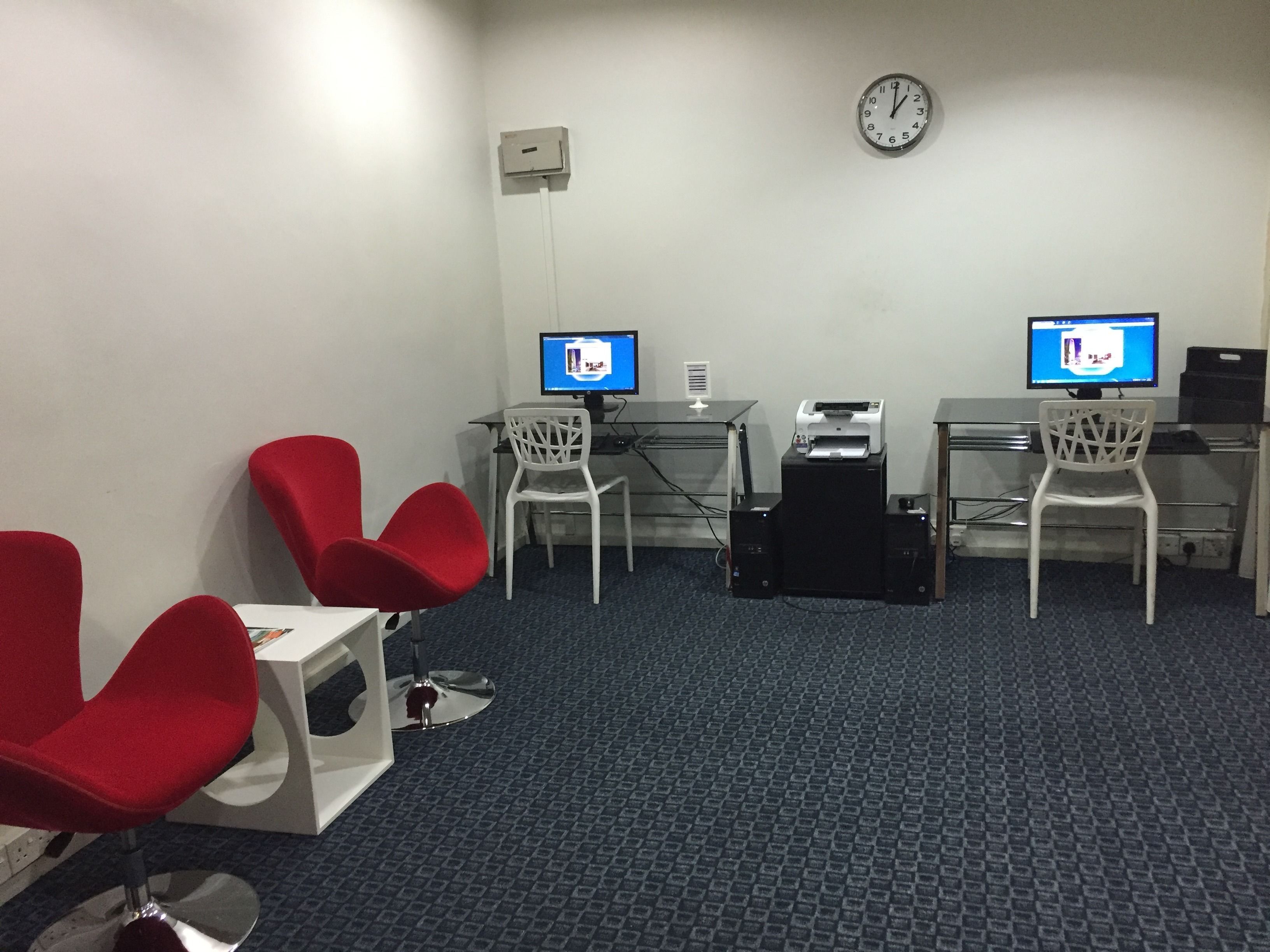 A room with two desks, two chairs, a clock, and a printer.