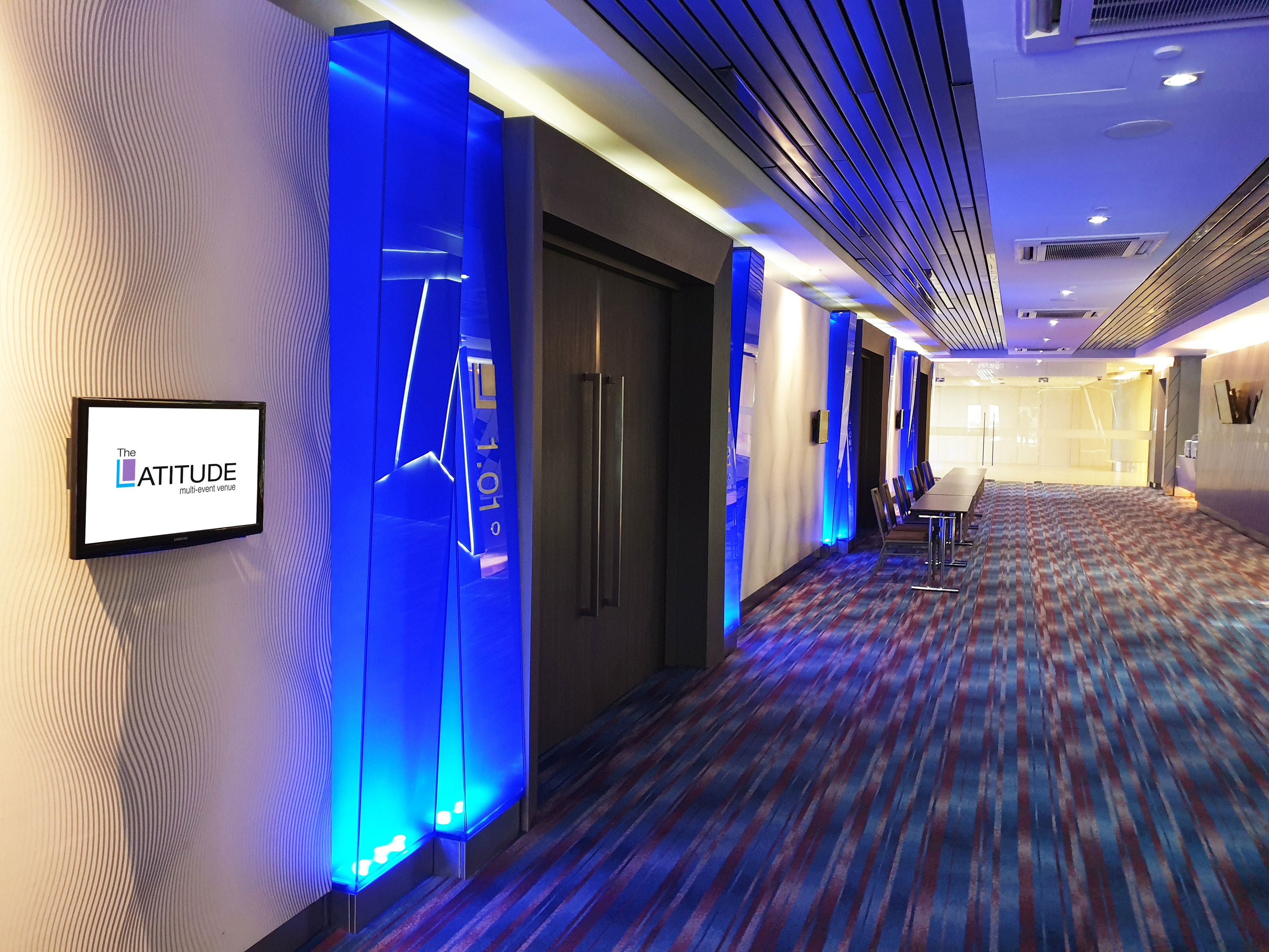 Un pasillo de hotel con una recepci ón iluminada en azul, una sala de conferencias y una alfombra estampada.