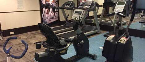 Un gimnasio con cintas de correr, elíptica y bicicleta estática.