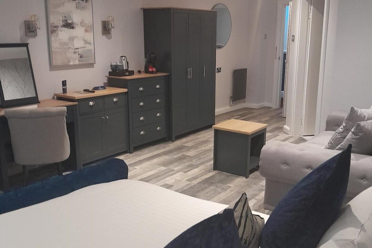 A modern bedroom with a large bed, a desk, a wardrobe, and a small table.