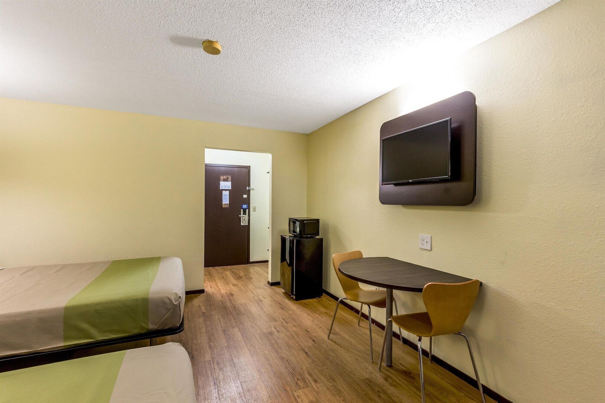 A hotel room with a bed, a desk with a chair, a television, and a door.