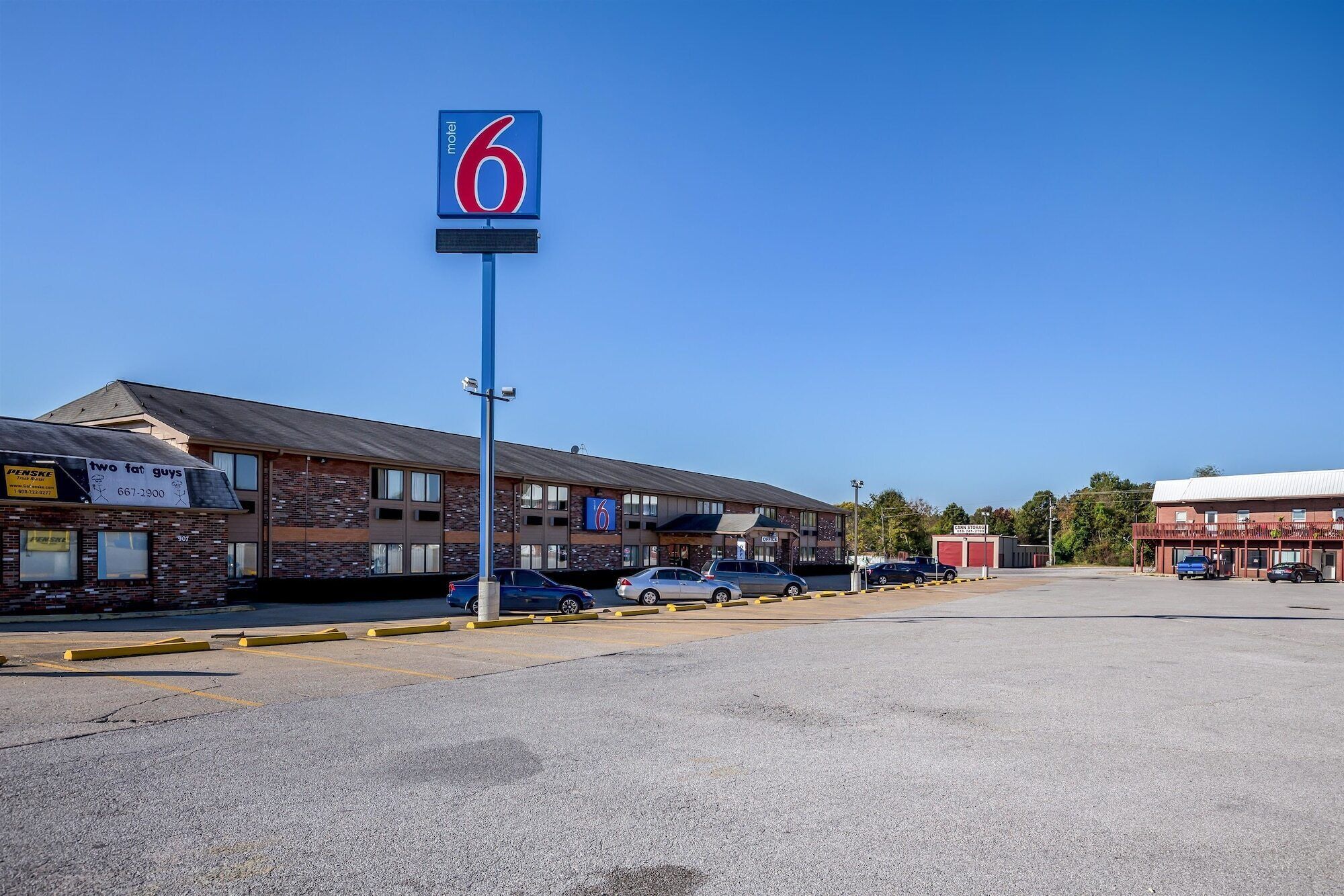 Un motel avec un grand panneau indiquant le chiffre « 6 », un parking et un bâtiment sur lequel on peut lire l’inscription « deux gros types ».