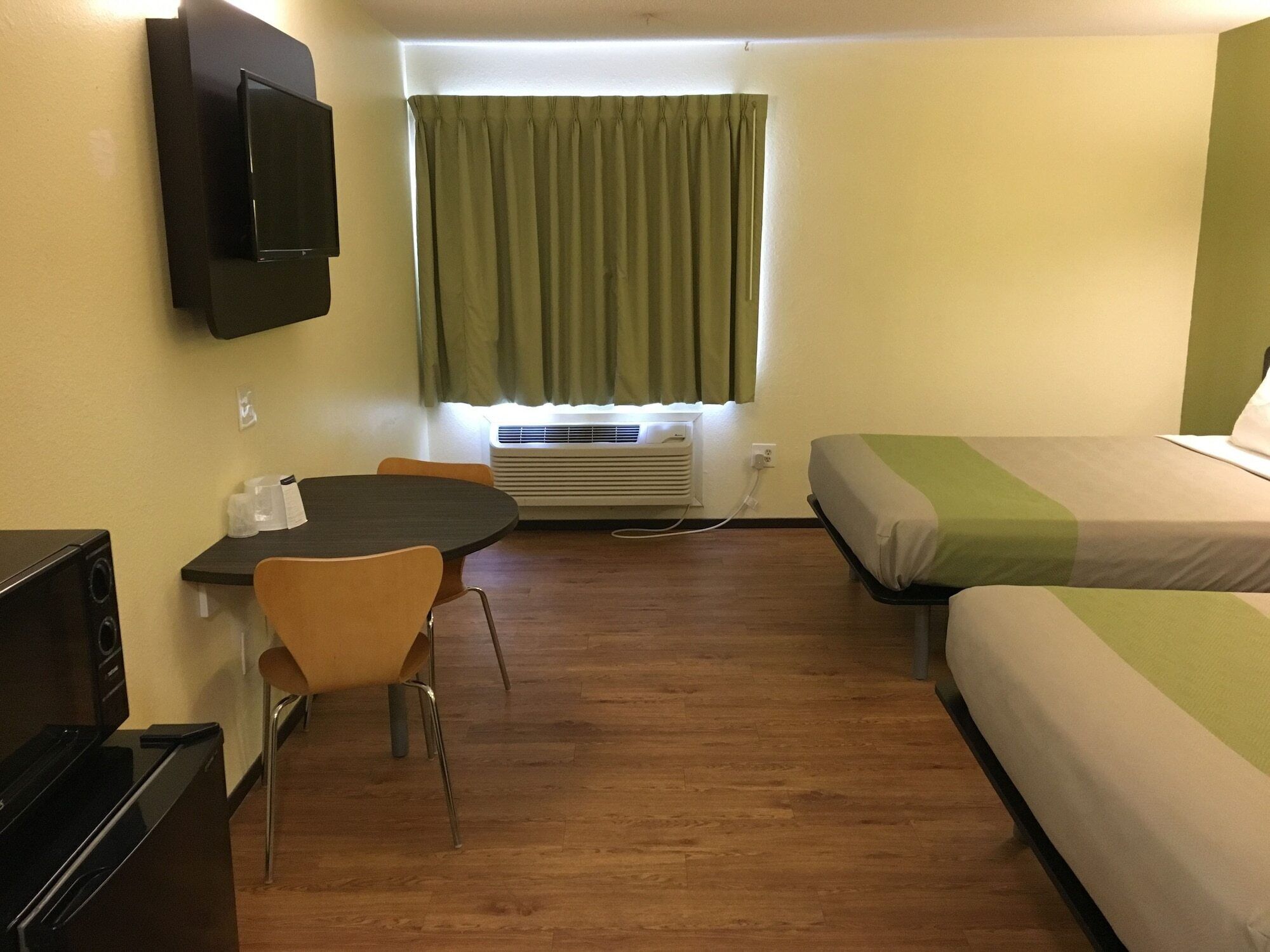 A hotel room with a bed, a desk with a chair, a television, and an air conditioning unit.