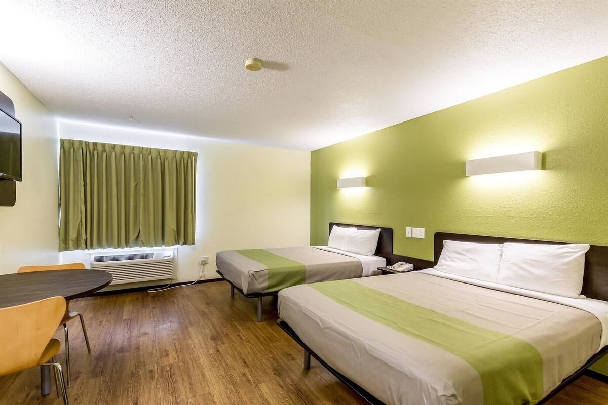 A hotel room with two beds, a desk, a chair, a TV, and a window with curtains.