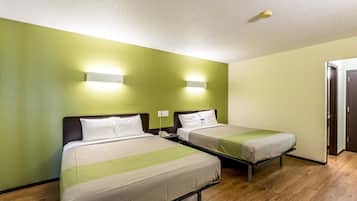 Habitación de hotel con dos camas individuales, paredes verdes, suelo de madera y una puerta a la derecha.