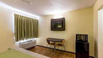 A small room with a bed, a table with two chairs, a TV mounted on the wall, and a refrigerator.