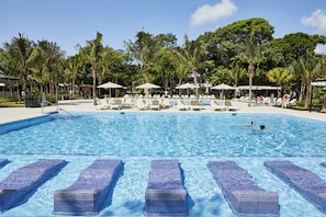 A swimming pool with lounge chairs and umbrellas, surrounded by palm trees.