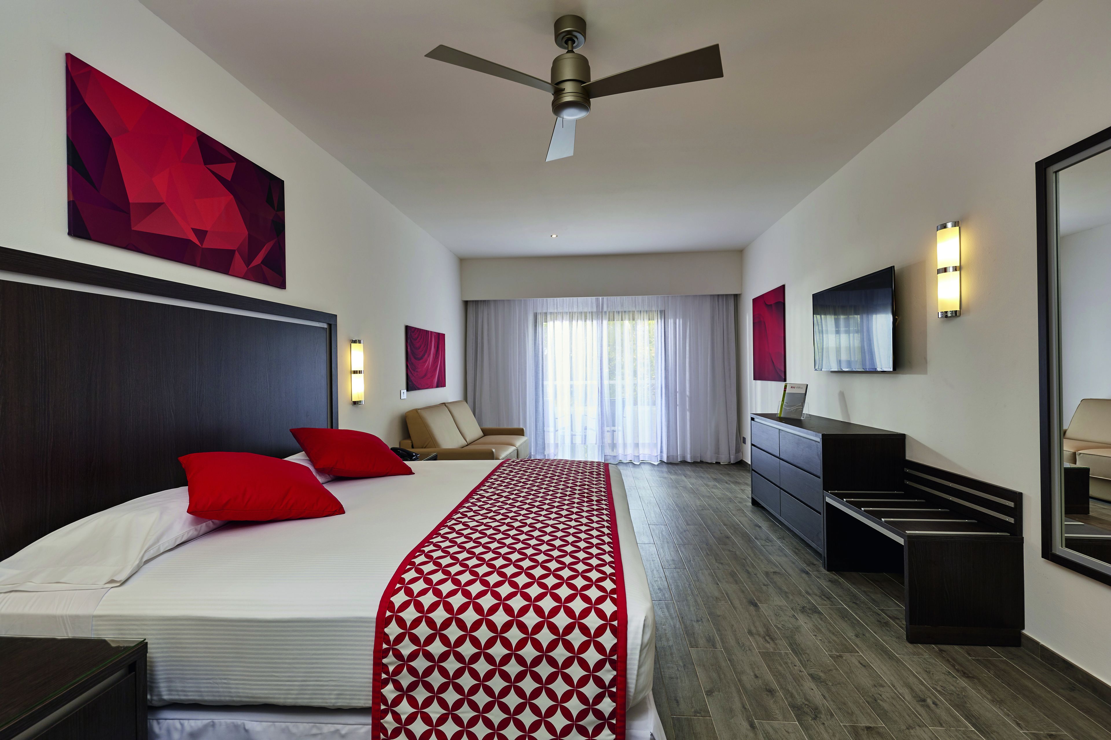 A modern hotel room with a large bed, a ceiling fan, a desk, and a wardrobe.