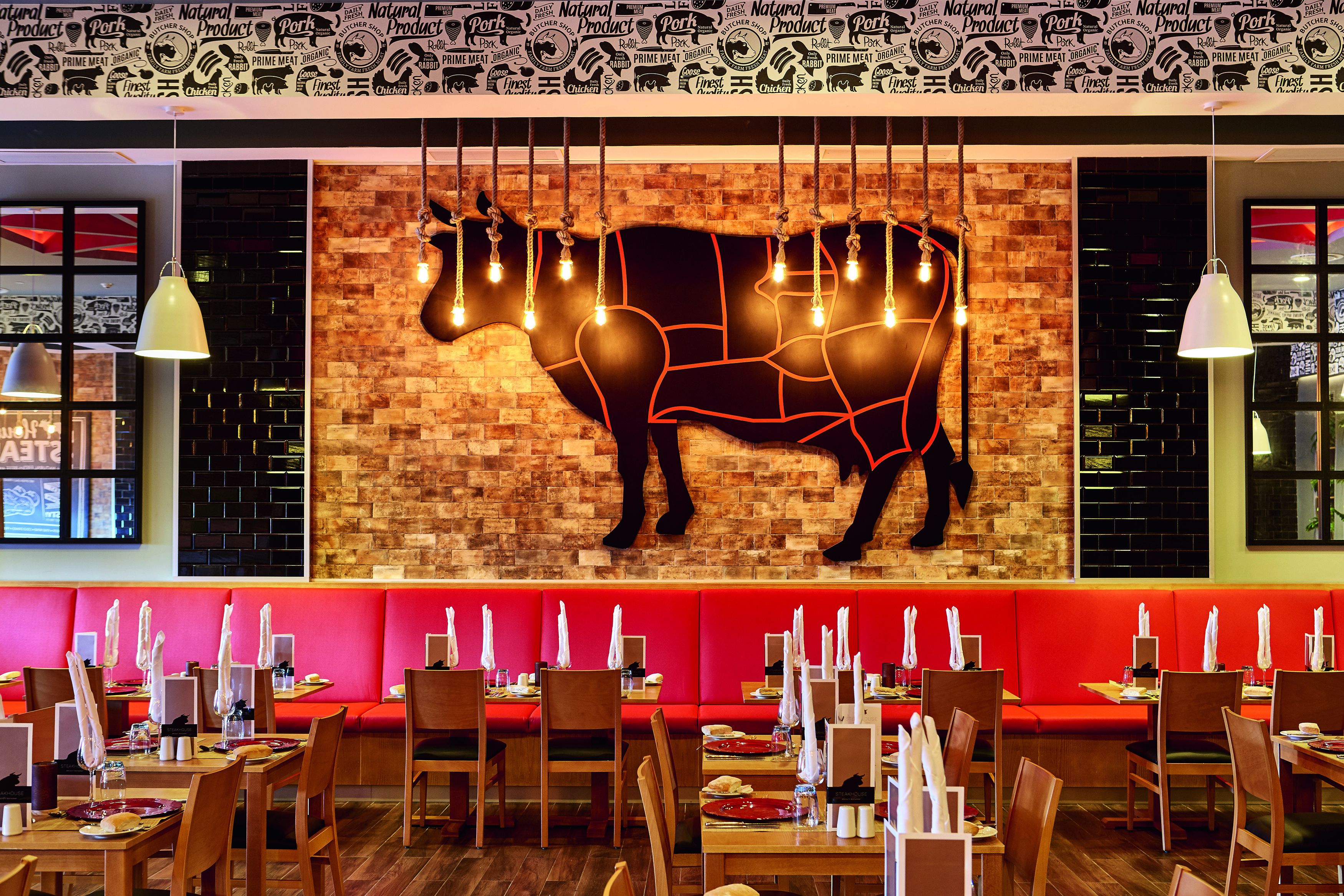 A restaurant with a brick wall and a large cow silhouette. Tables are set with white napkins and plates.
