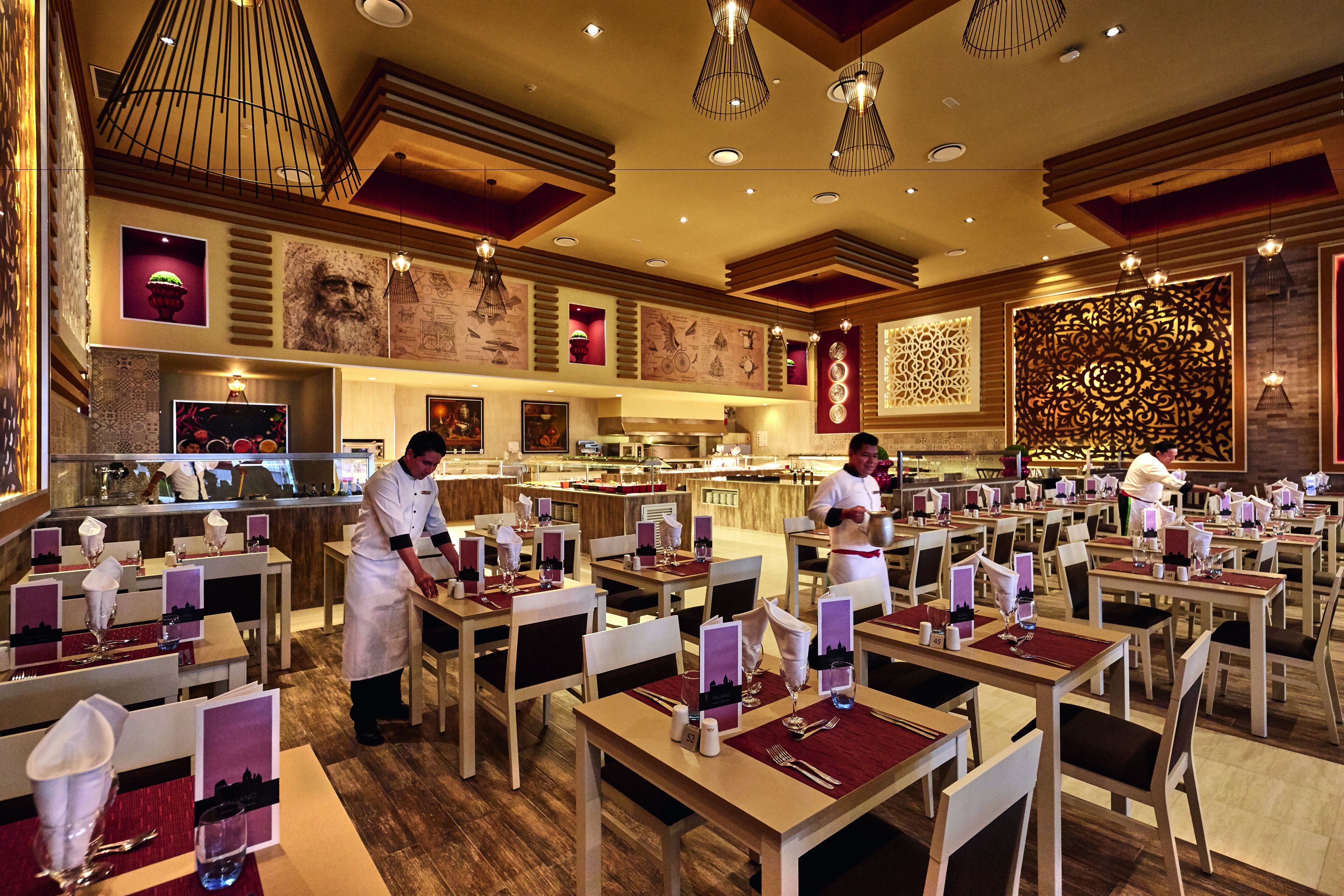 Ein Restaurant mit mehreren Tischen, gedeckt mit Besteck und Servietten, und Kellnern in weißen Uniformen.
