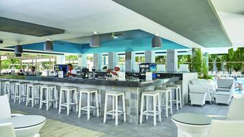 A bar area with white bar stools, a counter with a bartender, and outdoor seating with white wicker furniture.