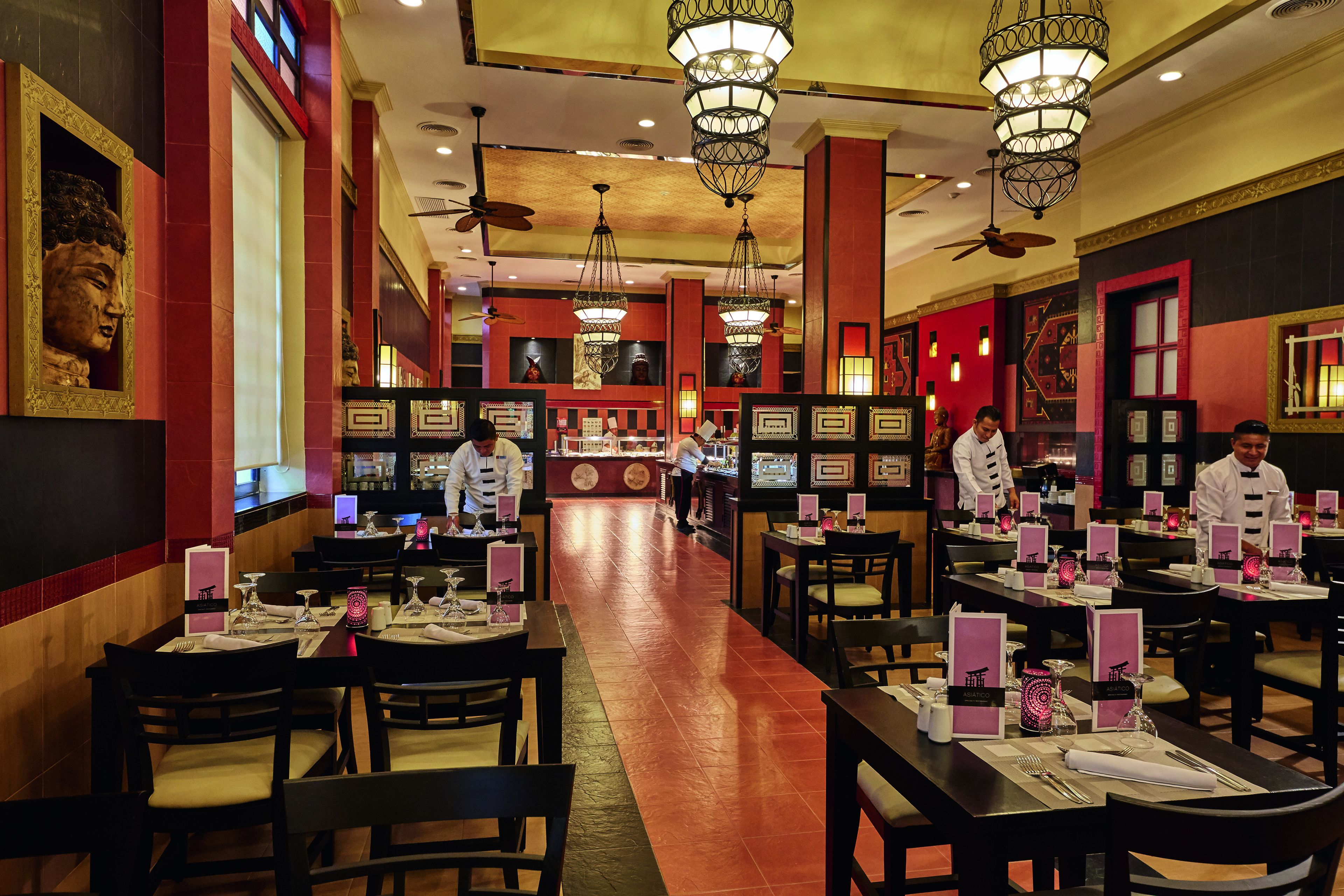 A restaurant with multiple dining tables, chairs, and hanging chandeliers.