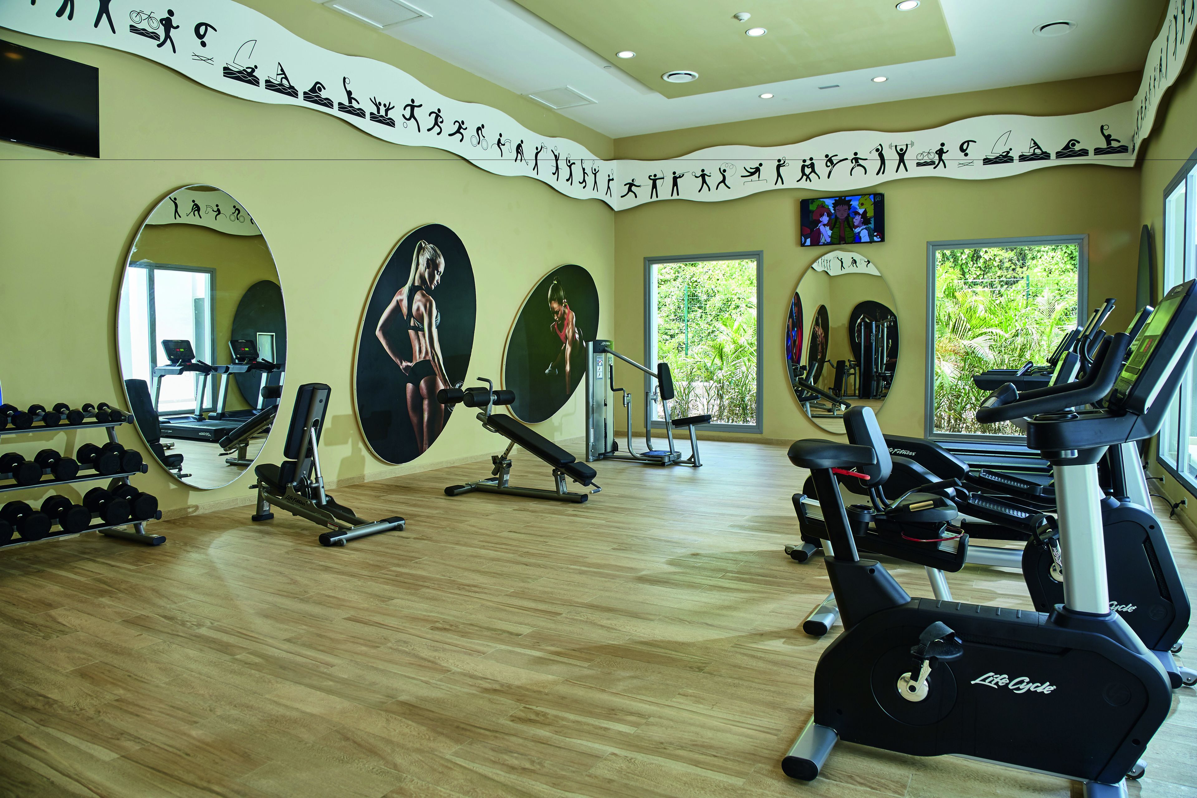 A gym with exercise equipment, mirrors, and a wall with motivational text.