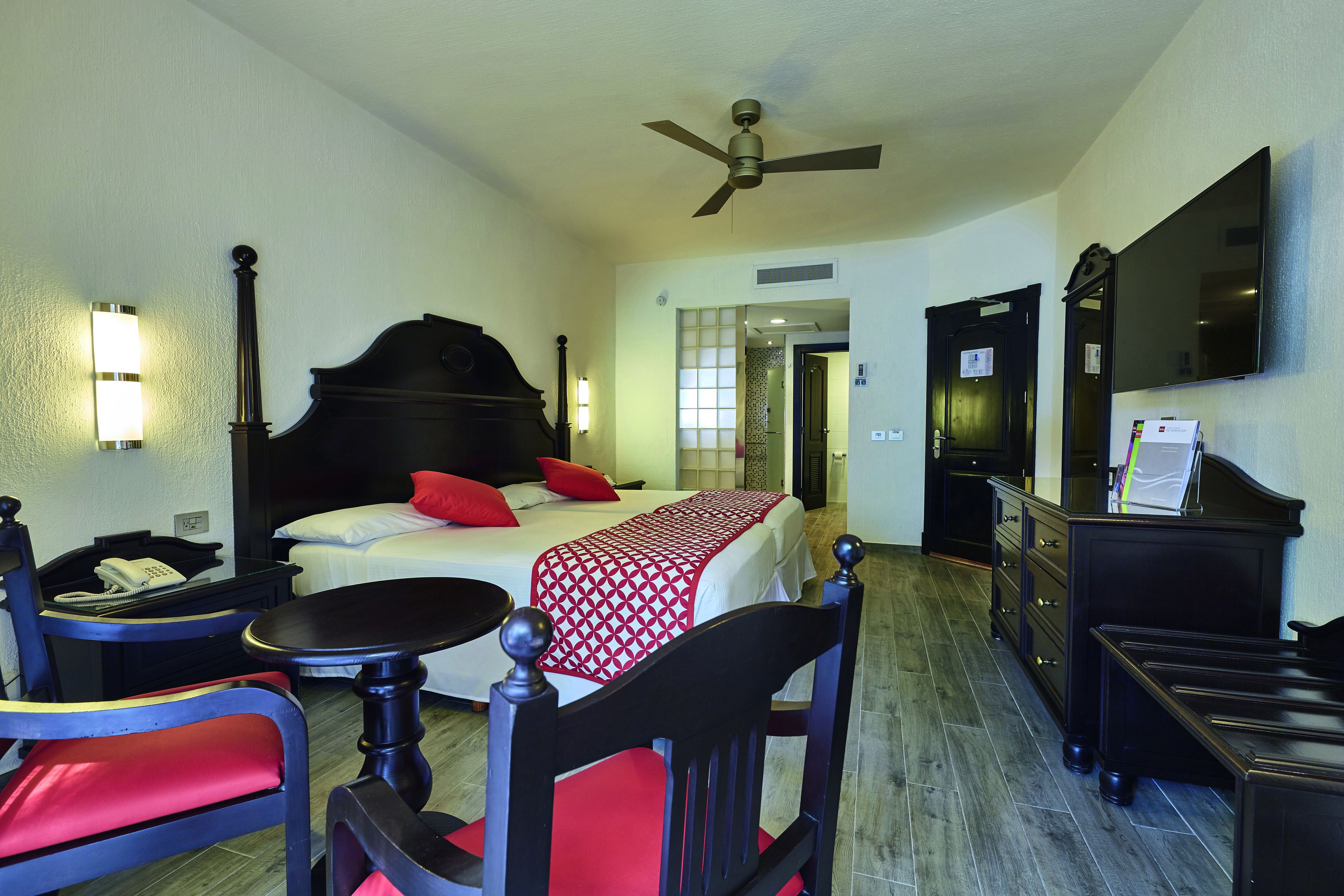 Une chambre d’hôtel équipée d’un lit, d’un bureau, d’une chaise, d’une télévision et d’un ventilateur de plafond.