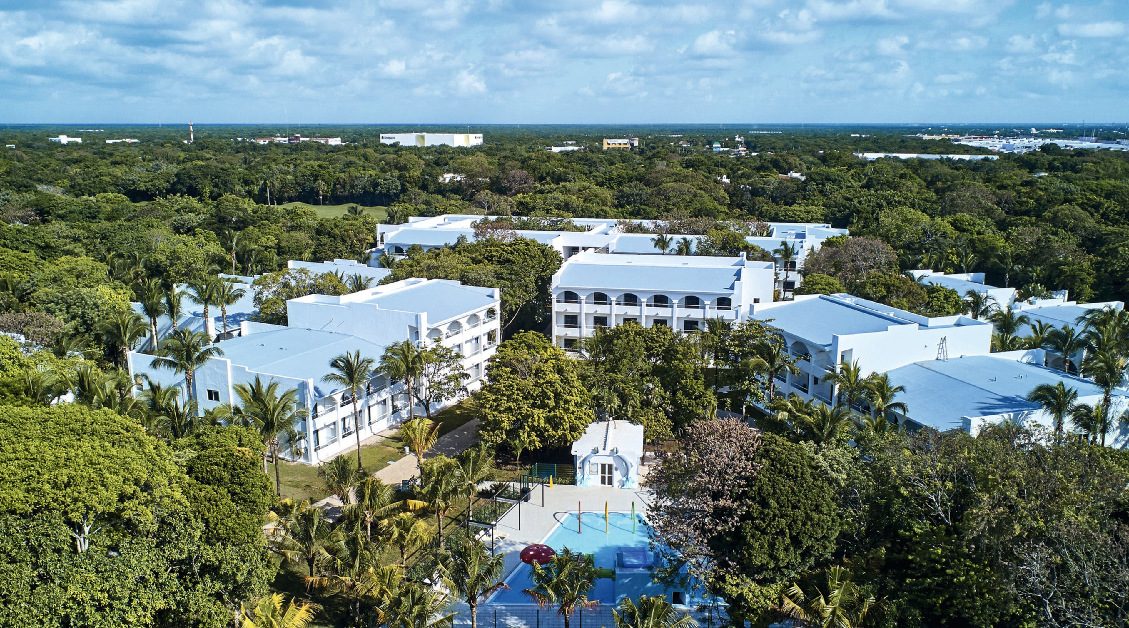 Un resort con varias edificaciones, piscina y abundante vegetación.
