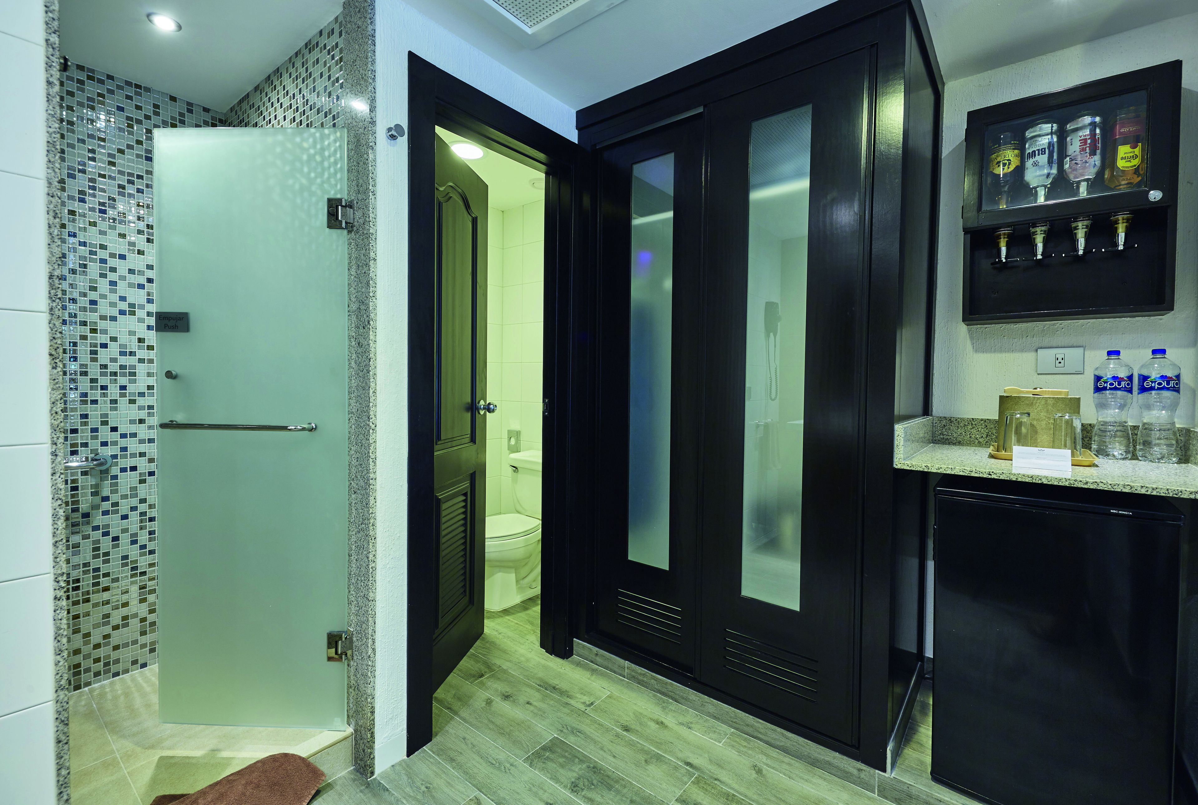 Een moderne badkamer met een douchecabine van glas, een toilet en een zwart kastje met waterdispenser.