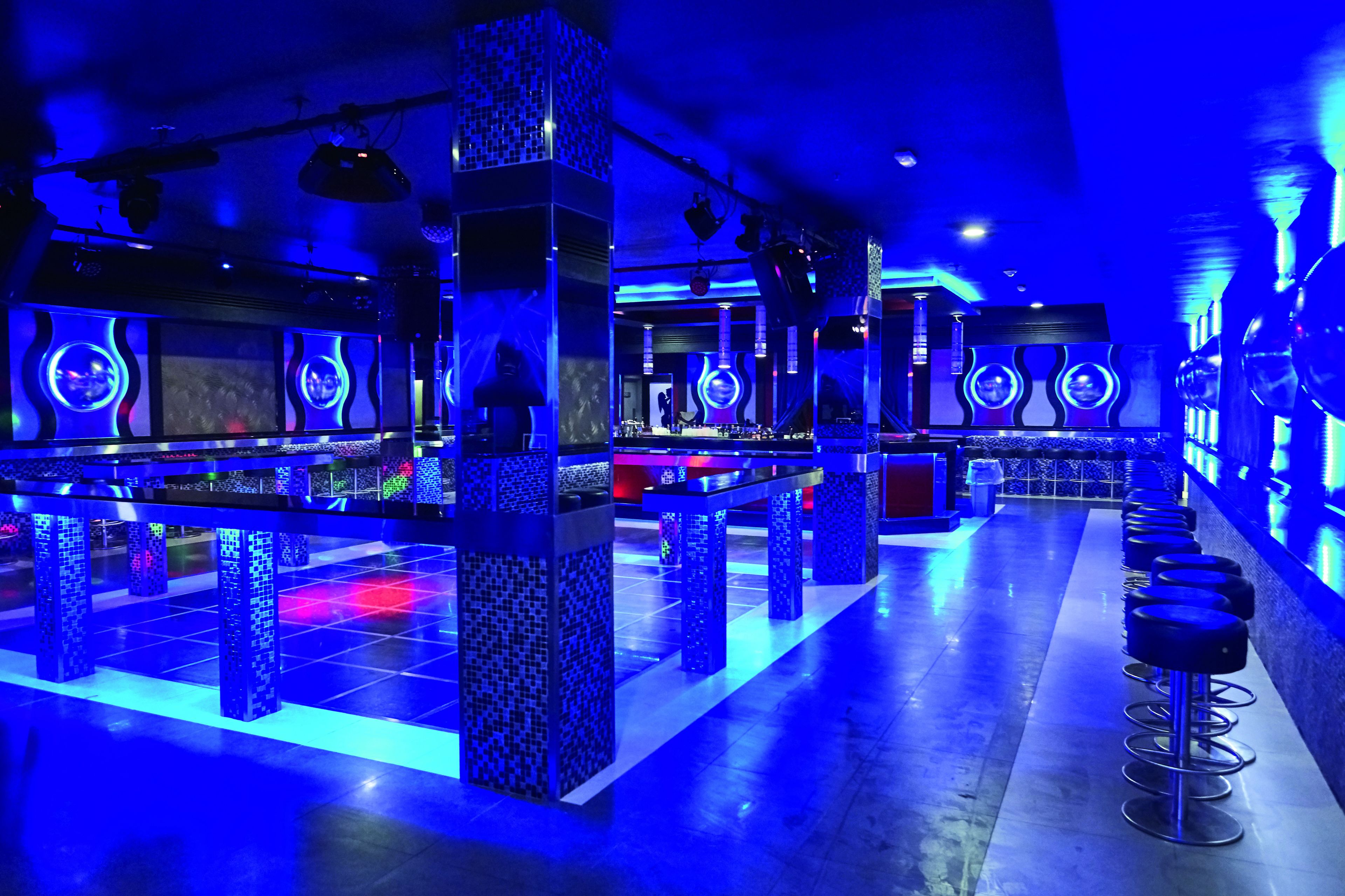 Zona bar con illuminazione blu, sgabelli e tavolo da biliardo.