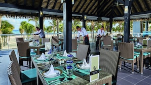 A restaurant with outdoor seating overlooking the beach, featuring wicker furniture and a tropical ambiance.
