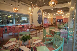 A restaurant with colorful chairs and tables, a large wall art piece, and hanging lights.